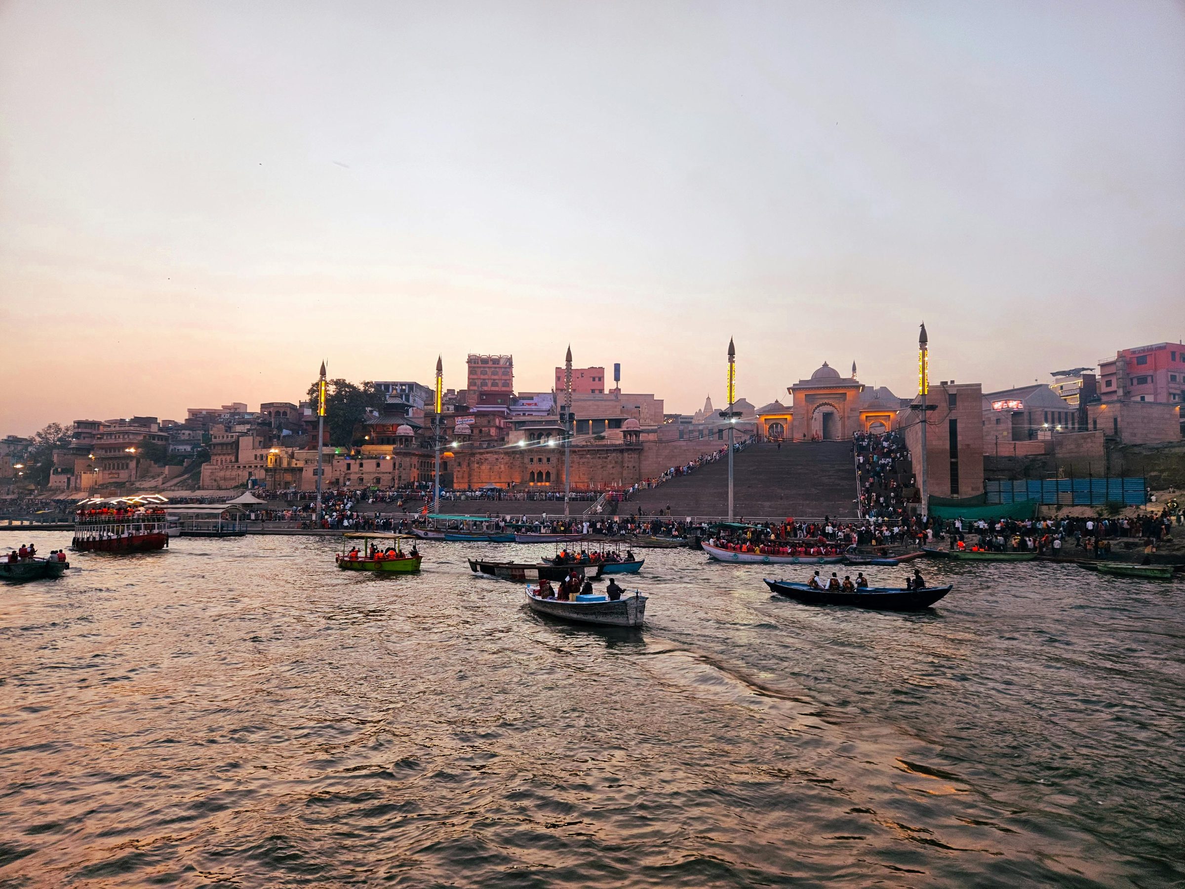 The ghats at dusk, the steps already full, boats gathering on the river below