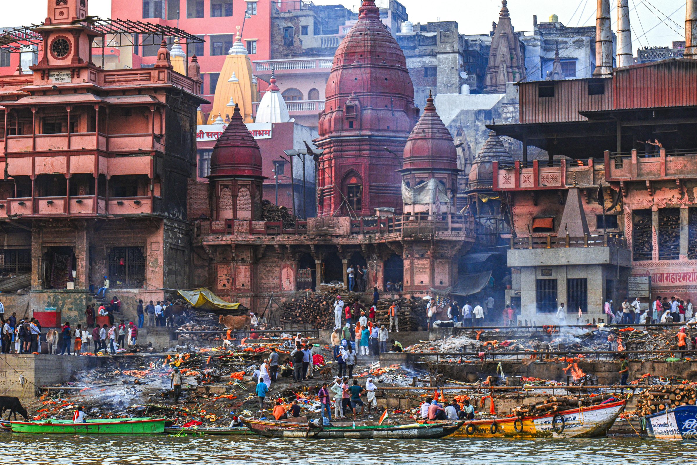 Manikarnika Ghat from the water: red temple spires, woodpiles and boats